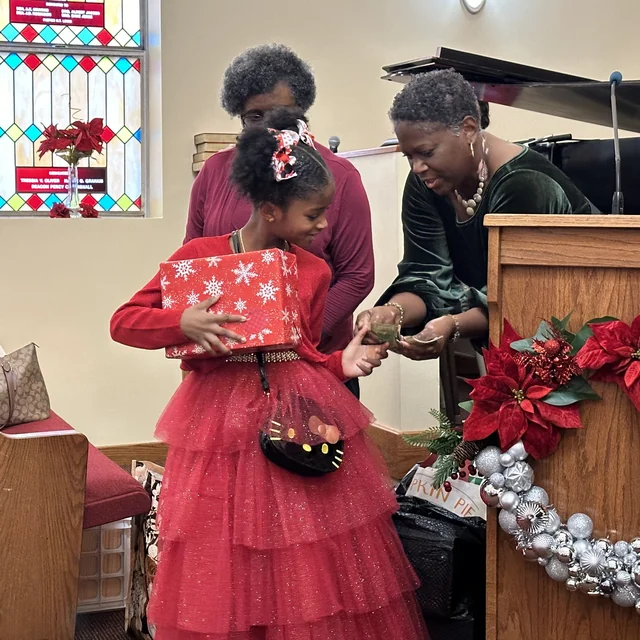 A child and two adults sharing a holiday gift moment in Second Baptist’s sanctuary.